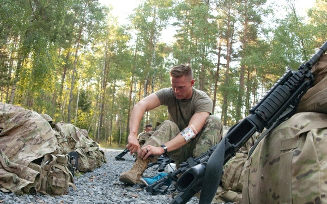 Soldier tying tactical boots at campsite